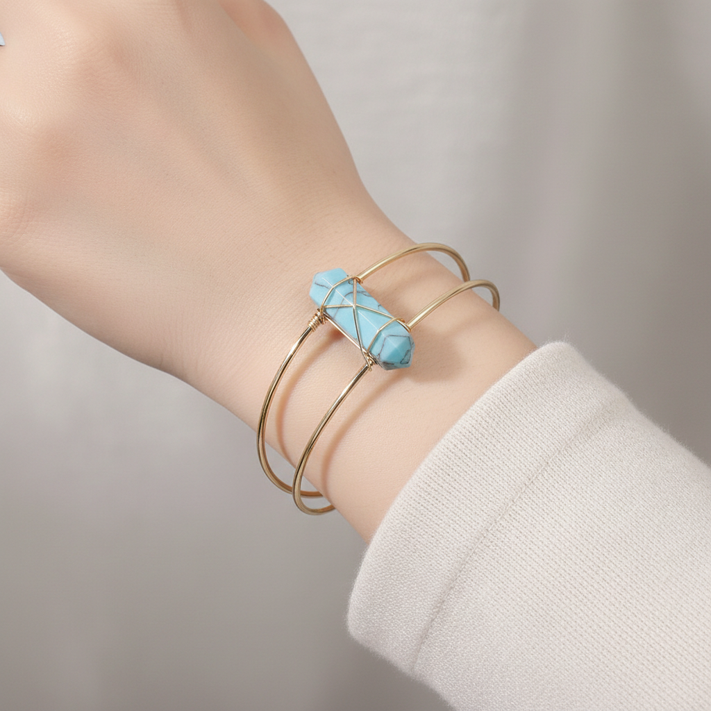 Gold wire cuff bracelet with pale blue faceted stone worn on a wrist