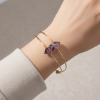 Gold wire cuff bracelet with purple faceted stone worn on a wrist