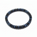Blue tiger eye bracelet laid in a loose curve with raking light emphasizing the blue chatoyancy across the black faceted beads