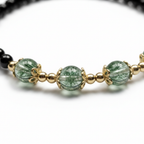 Macro detail of black obsidian and green phantom crystal bracelet showing natural inclusions and gold-tone hand-wrapped details